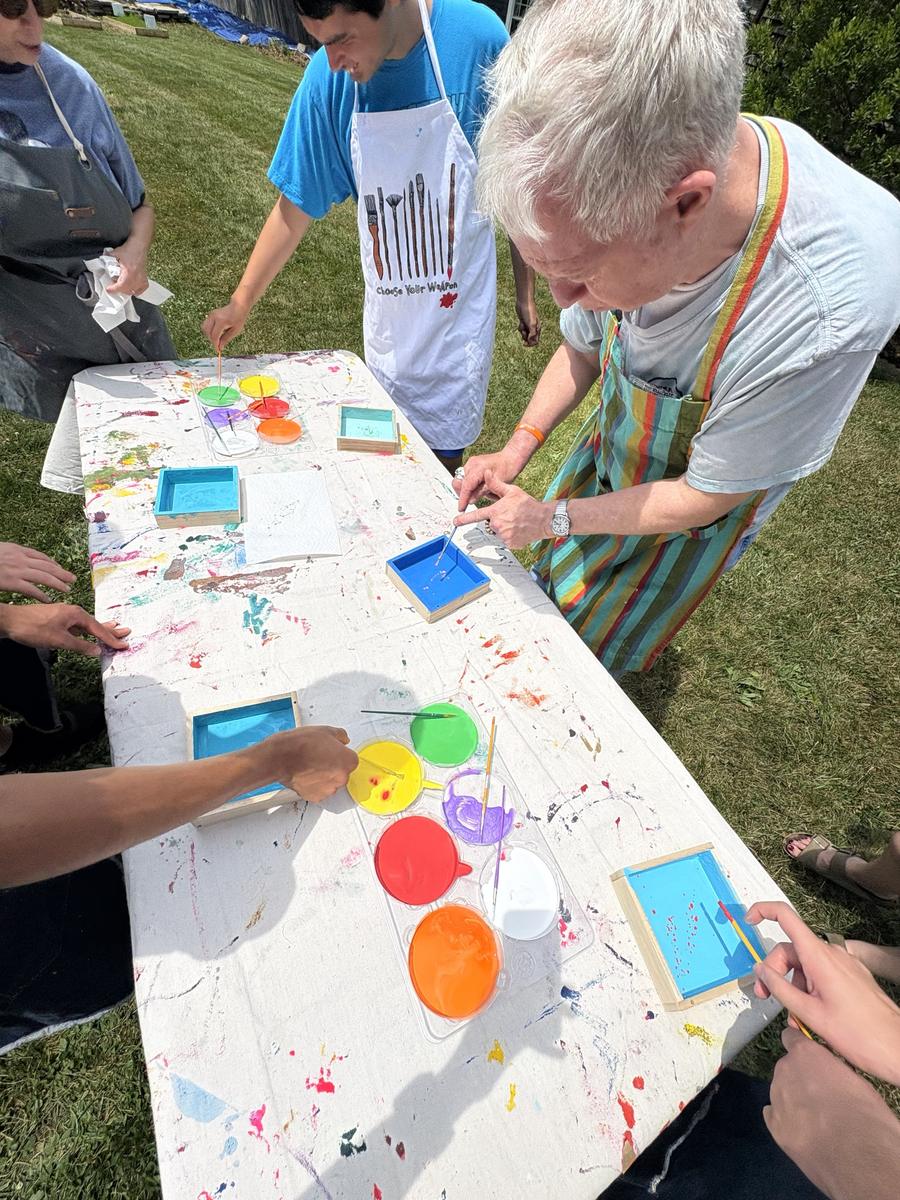 Members painting colorful wooden boxes together at an outdoor art club